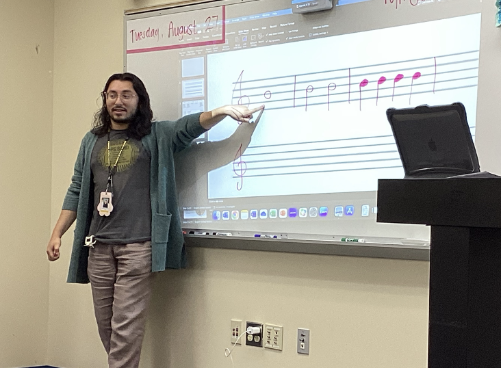 Mr. Sanchez teaches his first hour music class, by pointing to each note on the board. He asks his class what note is displayed, then he says what note it is.