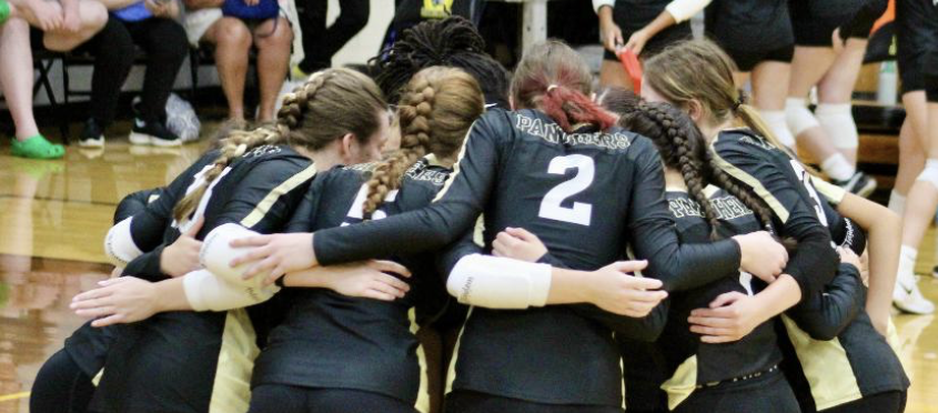 The volleyball team huddles up,  communicating the strategy for the next play.