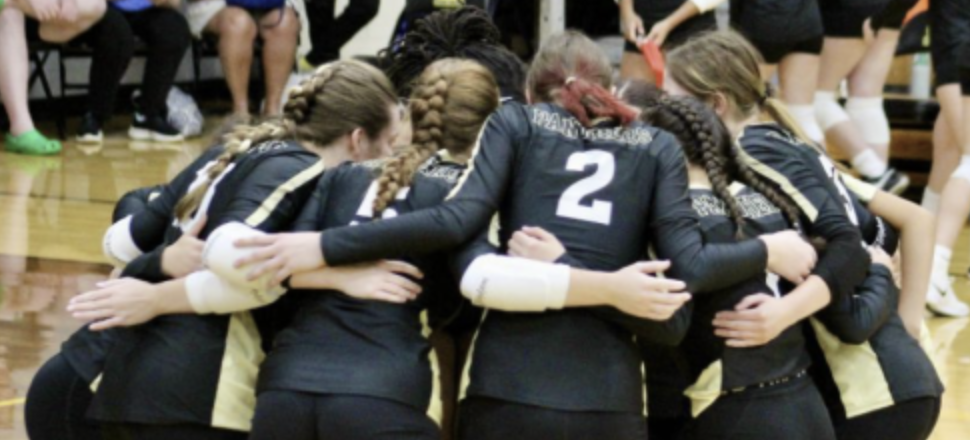 The volleyball team huddles up, communicating the strategy for the next play.